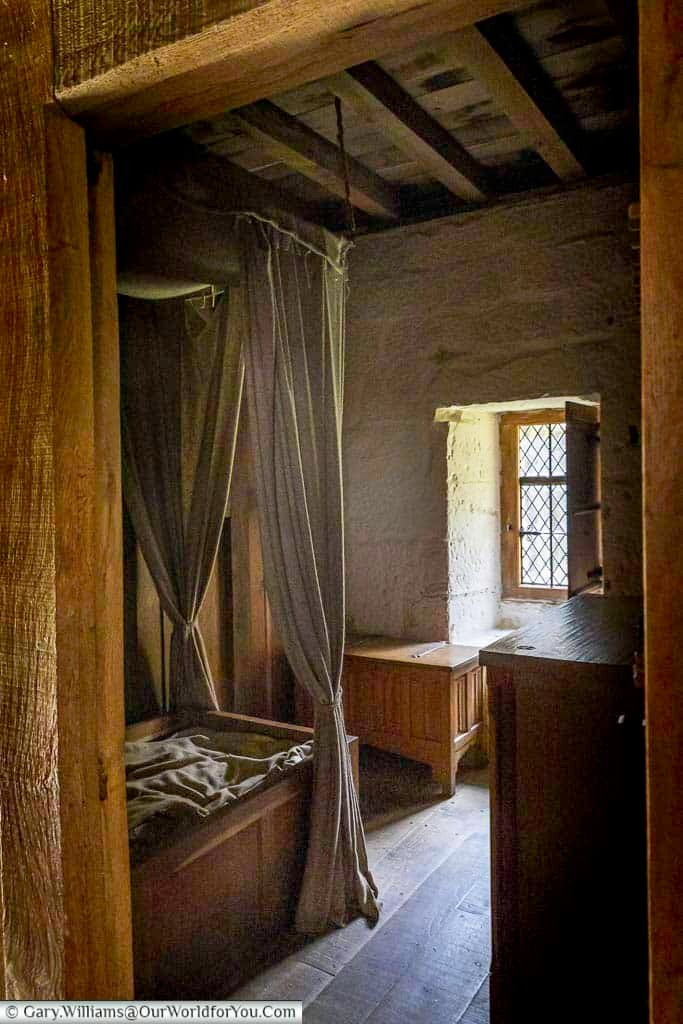 A simple medieval monk’s bedroom at Mount Grace Priory, featuring a wooden bed and leaded glass window letting in soft natural light. This preserved Carthusian cell offers a fascinating glimpse into monastic life in historic Yorkshire.