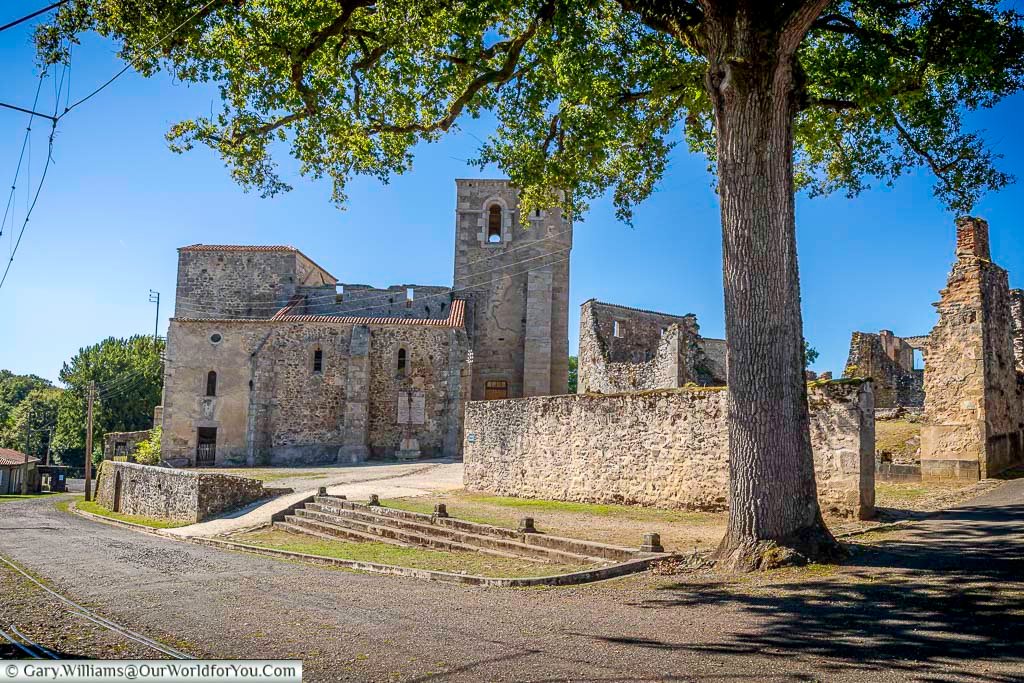 The ruins of the old Saint-Martin Church in Oradour-sur-Glane, framed by a large tree and surrounded by the remains of the destroyed village. This haunting historic landmark is one of the most moving places to visit in Oradour-sur-Glane, France.