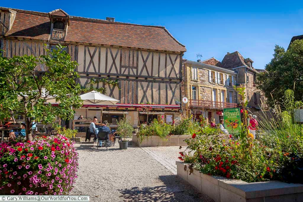 A charming view of Place de la Mirpe in Bergerac, featuring historic half-timbered houses, outdoor café seating, and vibrant flower displays. This picturesque square is one of the most beautiful places to visit in Bergerac, Dordogne.