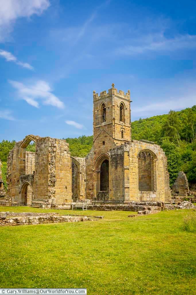 The impressive ruins of Mount Grace Priory church, with weathered stone arches and a tall medieval tower set against the green hills of North Yorkshire. This historic monastic site is one of the most atmospheric places to visit in Yorkshire.