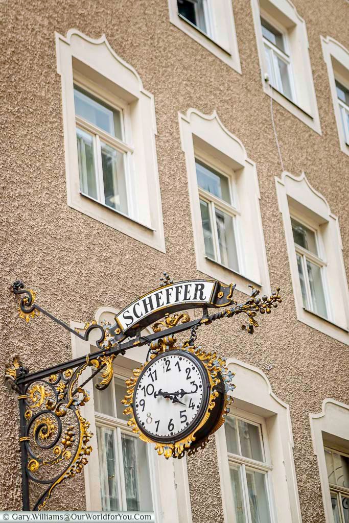 An ornate hanging clock and sign decorate a historic building along Getreidegasse in Salzburg. These decorative signs are a distinctive feature of the city’s Old Town streetscape.