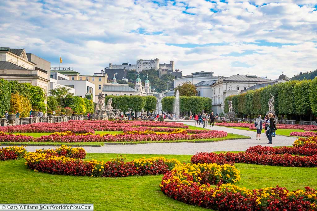 The Mirabell Palace Gardens in Salzburg with brightly coloured flower beds and fountain. In the distance, high on the hill, you can see the city's Castle.