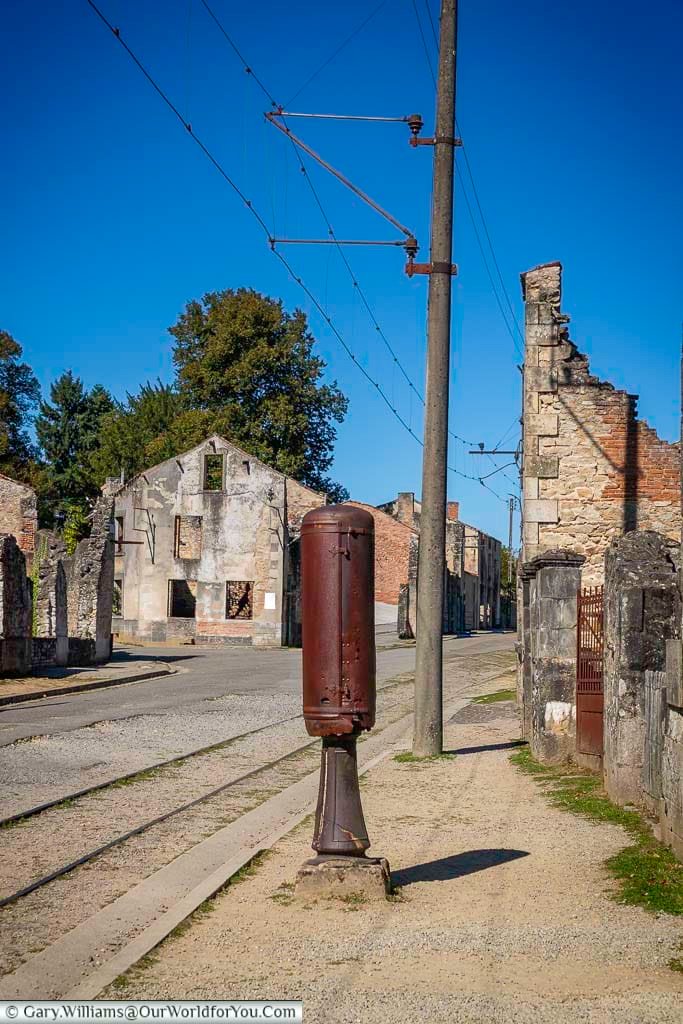 The railway tracks running through the ruins of Oradour-sur-Glane, with damaged buildings and overhead lines still in place. This haunting scene shows how the village was frozen in time as a World War II memorial in France.
