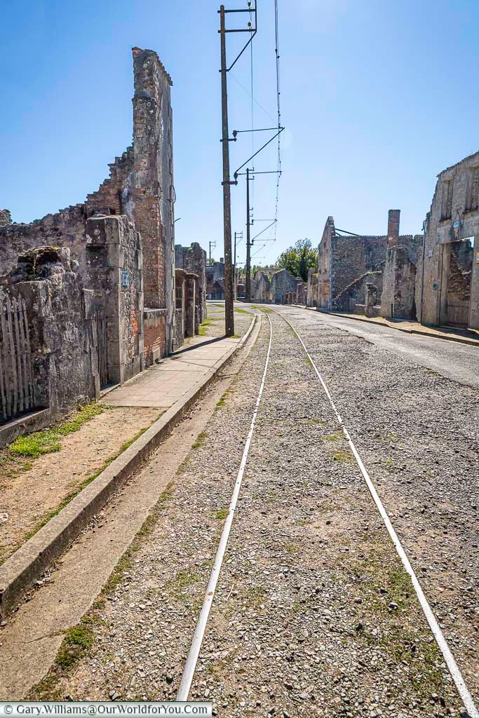 Old tram tracks run through the ruined streets of Oradour-sur-Glane, a preserved World War II memorial village in France. The rails guide visitors through the silent remains of homes and shops destroyed in 1944.