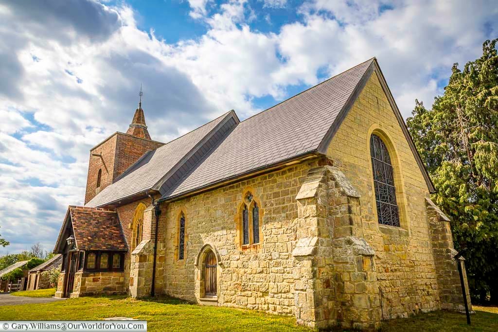 The exterior of All Saints’ Church in Tudeley, Kent, showcases a charming mix of stone and brick architecture under a dramatic sky. This historic village church is famous for housing the only complete set of Marc Chagall stained glass windows in the world.
