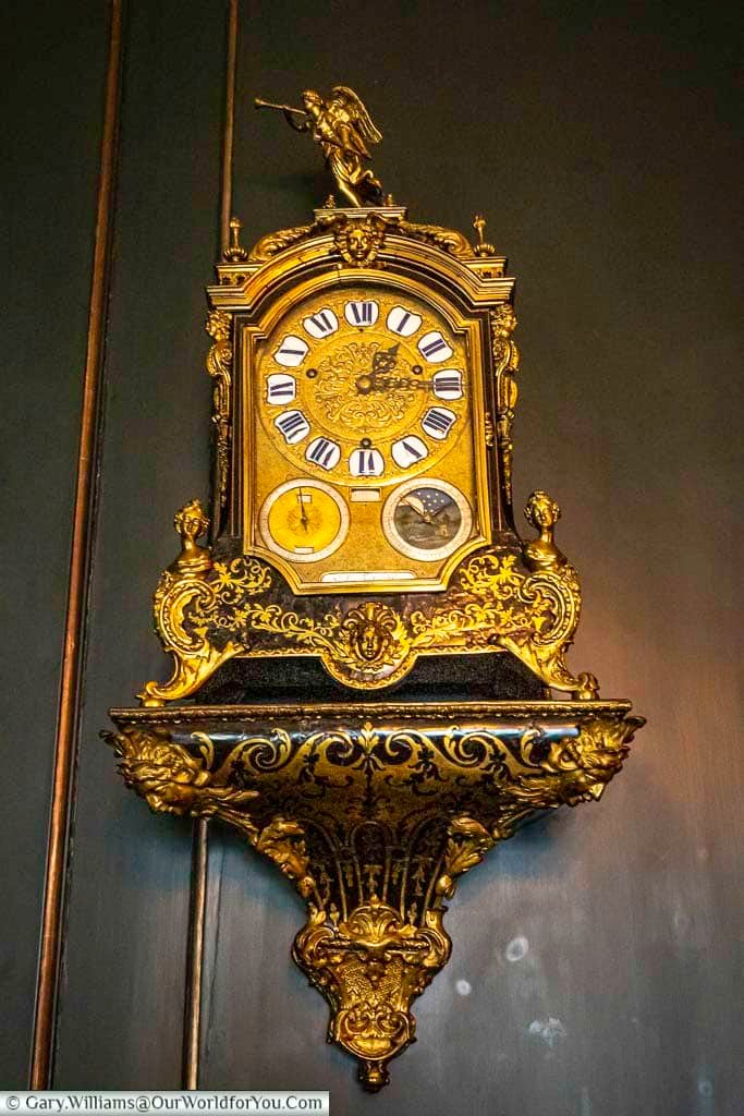 An ornate gilded bracket clock with Roman numerals sits against dark panelled walls inside the Treasurer’s House, York. The intricate gold detailing showcases the craftsmanship found within this historic York attraction.