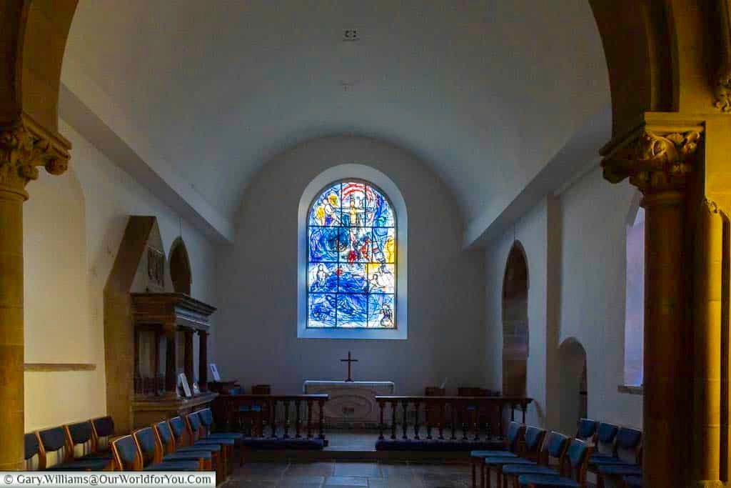 The intimate chapel of All Saints’ Church in Tudeley showcases beautiful stained glass windows by Marc Chagall above a simple altar and wooden seating. This tranquil interior is a hidden gem in Kent, blending history, art, and quiet reflection.