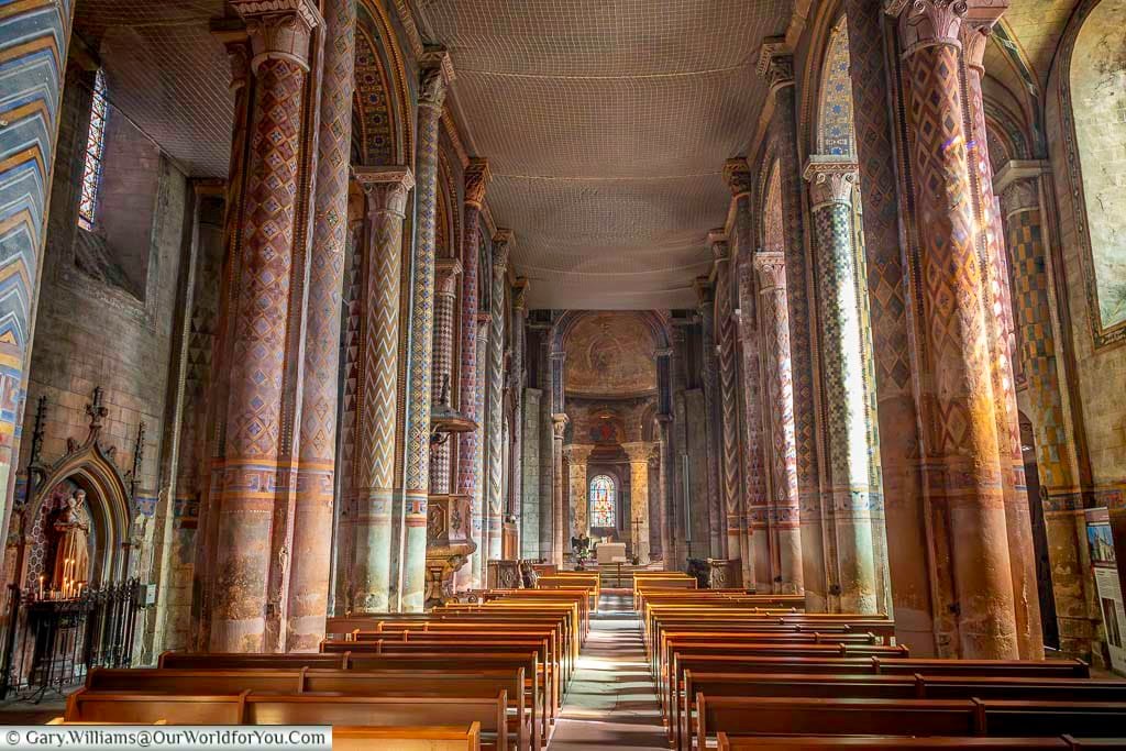 Colourful patterned columns and arches line the nave of a historic church in Poitiers, France. The vibrant medieval decoration and stained-glass windows create one of the most striking church interiors in the city.