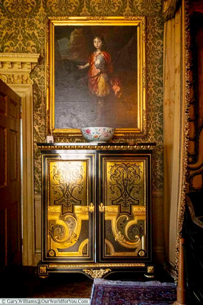 An elaborately decorated cabinet and framed portrait adorn the Queen’s Room at the Treasurer’s House in York. The gilded detailing and period furnishings highlight the refined interiors of this National Trust property in Yorkshire.