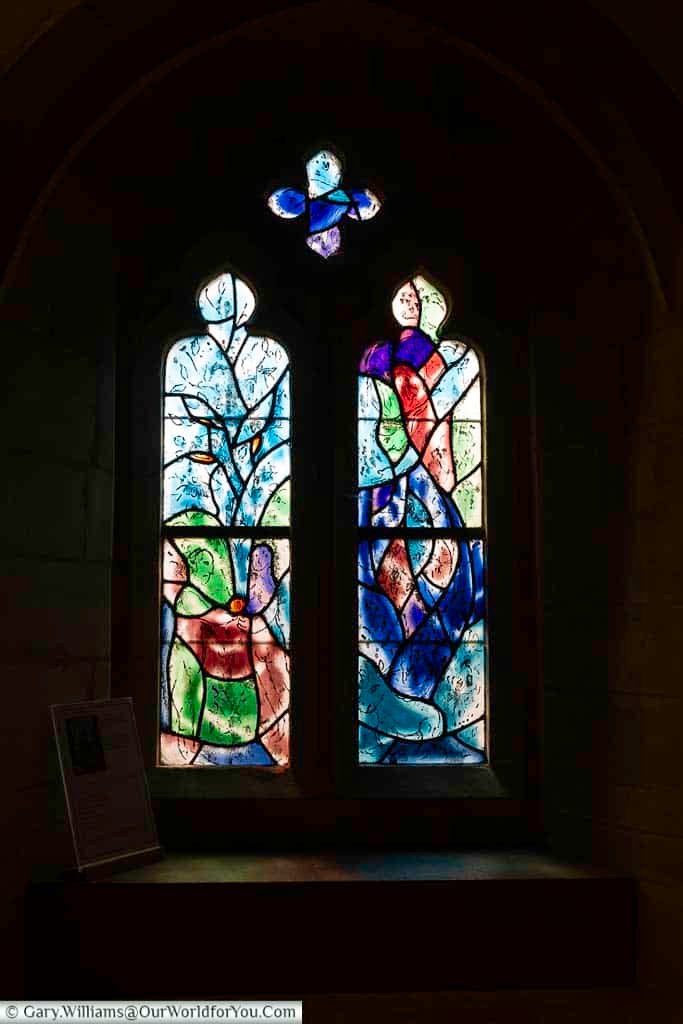 A striking stained glass panel by Marc Chagall depicts Eve offering the forbidden fruit to Adam in All Saints’ Church, Tudeley. This biblical scene is rendered in vibrant colours, making it one of the most captivating artworks in Kent.