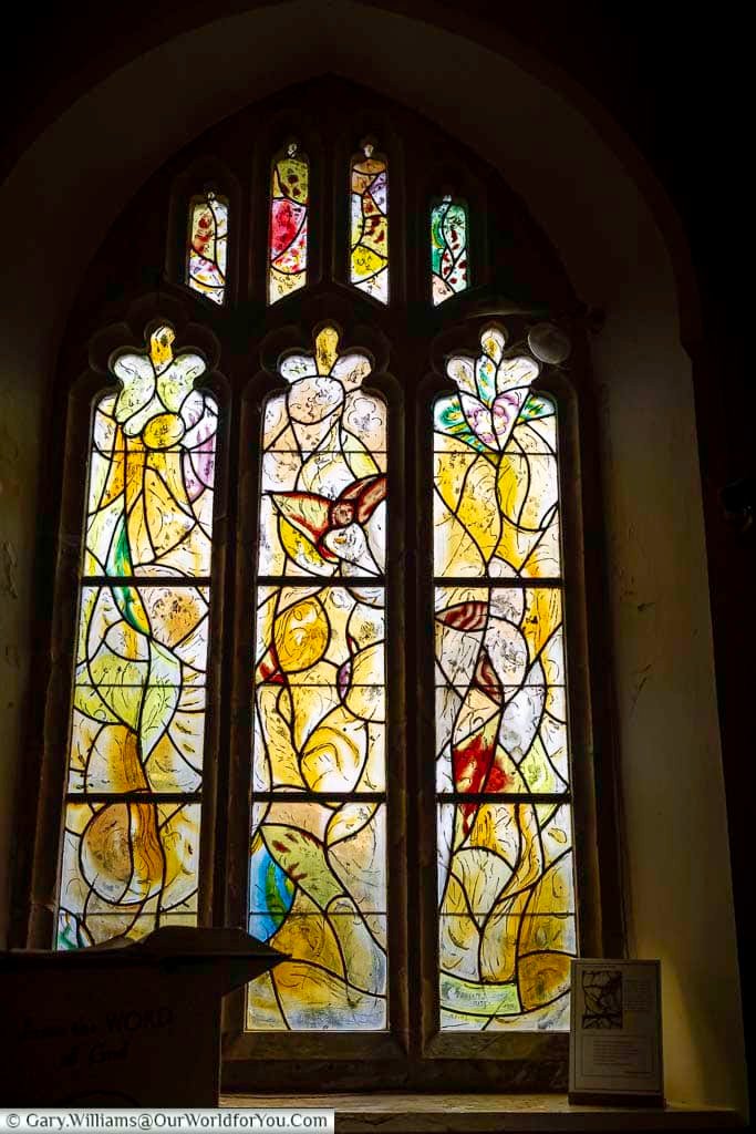 A luminous stained glass composition by Marc Chagall illustrates angels, birds, and symbolic elements in warm golden tones inside Tudeley Church. This extraordinary collection makes All Saints’ Church one of the most distinctive places to visit in England.