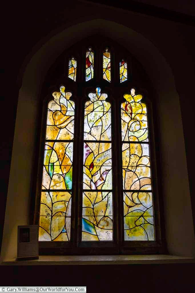 A vibrant Chagall stained glass window illustrates themes of resurrection with birds, a donkey, and symbolic candles in All Saints’ Church, Tudeley. This richly detailed artwork highlights why the church is considered one of the most unique places to visit in Kent.