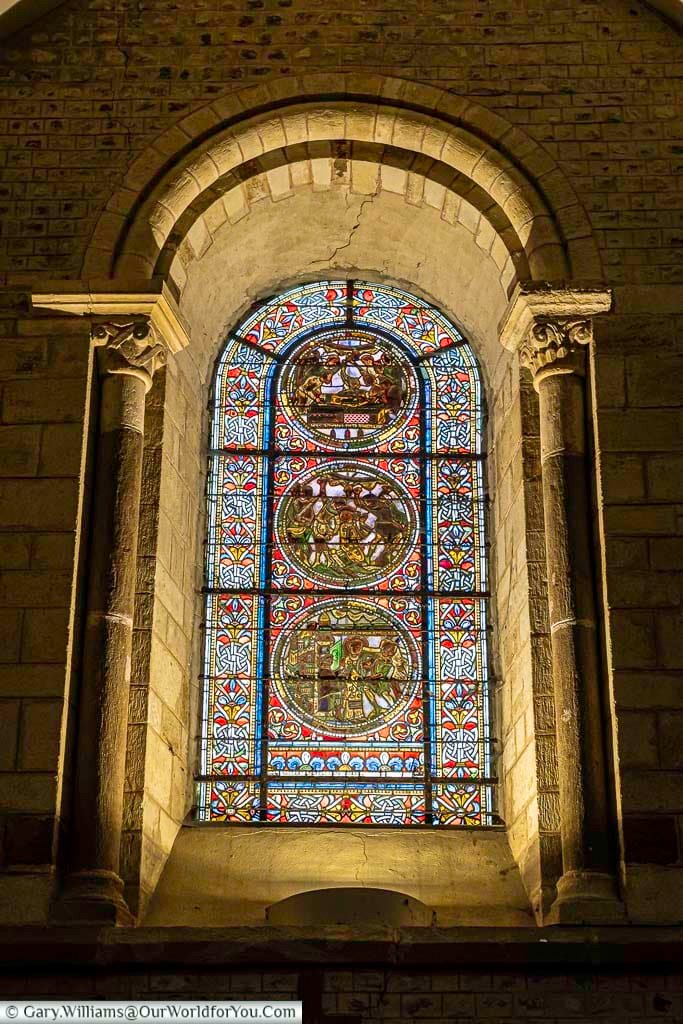 A stunning stained-glass window glows with vibrant colors inside a historic church in Le Mans, Pays de la Loire. The detailed biblical scenes and ornate stone arch highlight the craftsmanship of medieval French architecture.