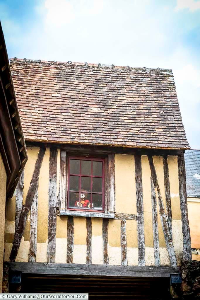Close-up of a traditional timber-framed house with a small window featuring a teddy bear in Le Mans’ historic quarter. The rustic beams and tiled roof highlight the unique medieval character of this French city.