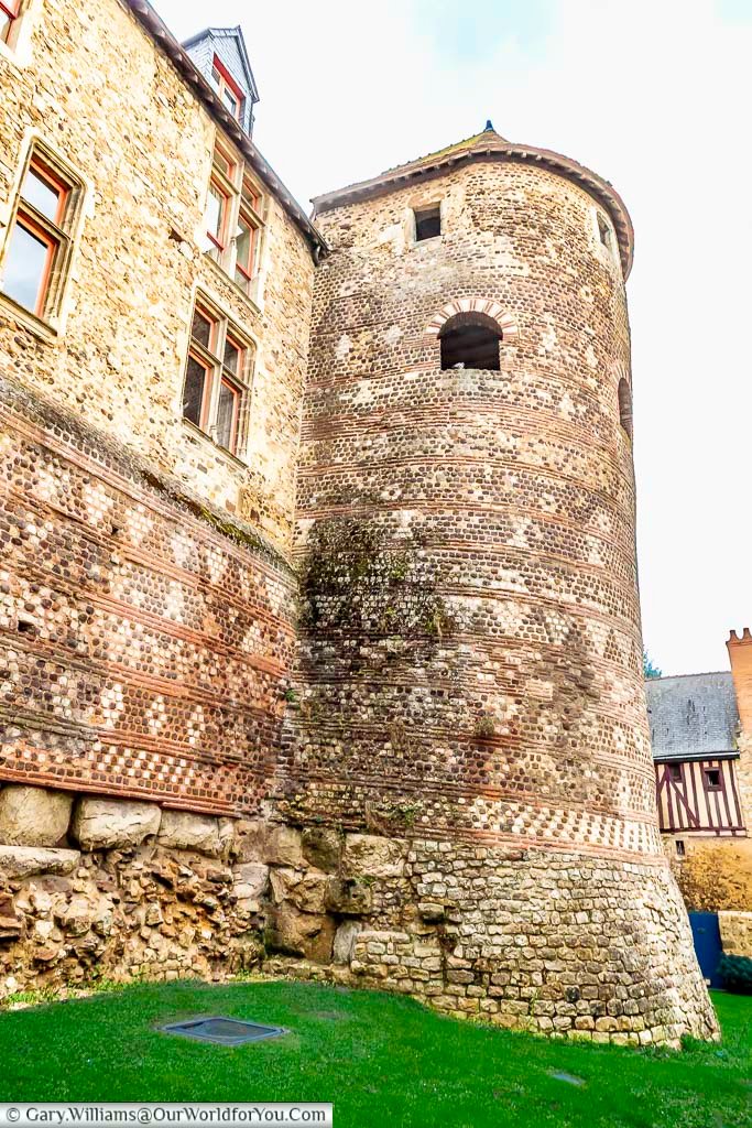 A rounded medieval tower rises above lush green grass and historic stone walls in Le Mans. This well-preserved structure highlights the architectural heritage of this iconic French destination.