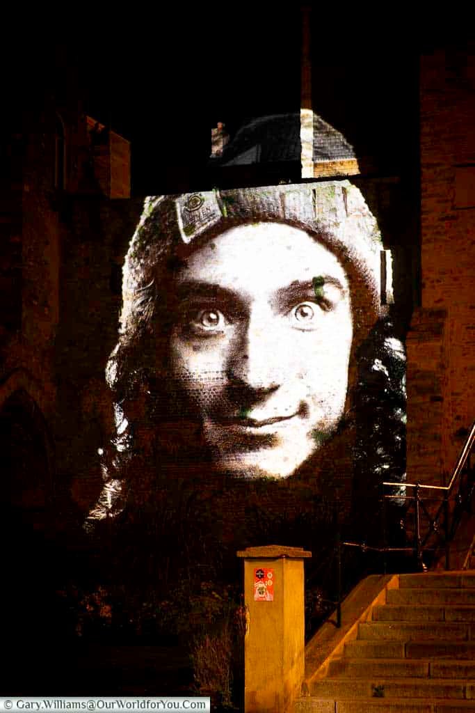 A dramatic black-and-white face projection lights up a historic building at night in Le Mans, France. This unique visual display is part of the city’s immersive light art experience.