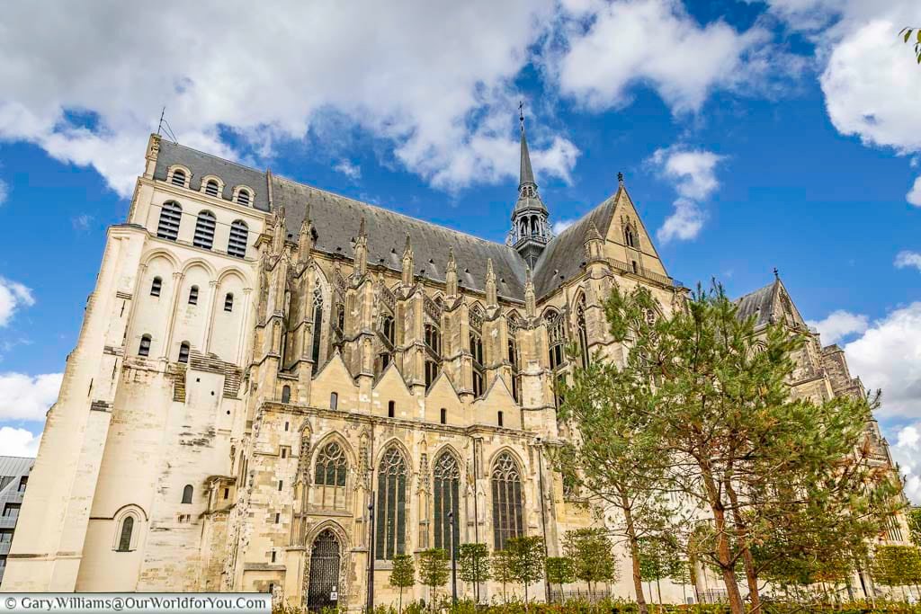 A stunning exterior view of the Gothic Basilique de Saint-Quentin reveals soaring stone architecture, detailed buttresses, and a dramatic spire beneath bright blue skies. This iconic cathedral is one of the top attractions in Hauts-de-France and a highlight of any Saint-Quentin sightseeing tour or French road trip.