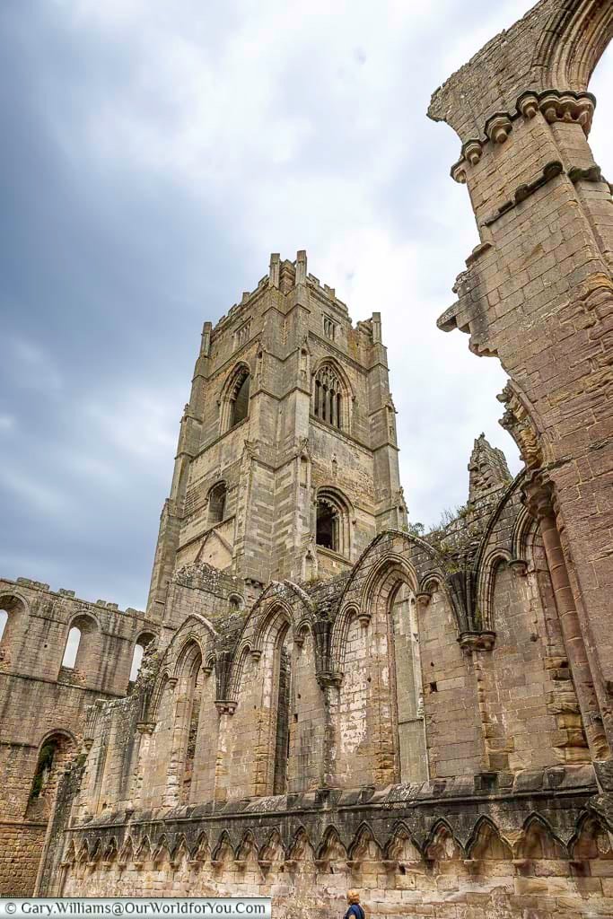 Dramatic view of the towering ruins of Fountains Abbey in North Yorkshire, showcasing Gothic stone arches and centuries of medieval history beneath a cloudy sky. The UNESCO World Heritage Site is one of the most iconic historic places to explore in England and a must-see destination in Yorkshire.