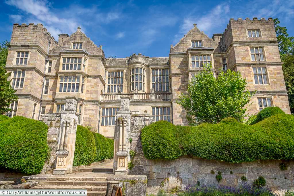 Elegant exterior view of Fountains Hall in Yorkshire, surrounded by manicured hedges and historic stone architecture under a bright blue sky. The Elizabethan manor house near Fountains Abbey is one of the most beautiful National Trust properties and historic places to visit in Yorkshire.