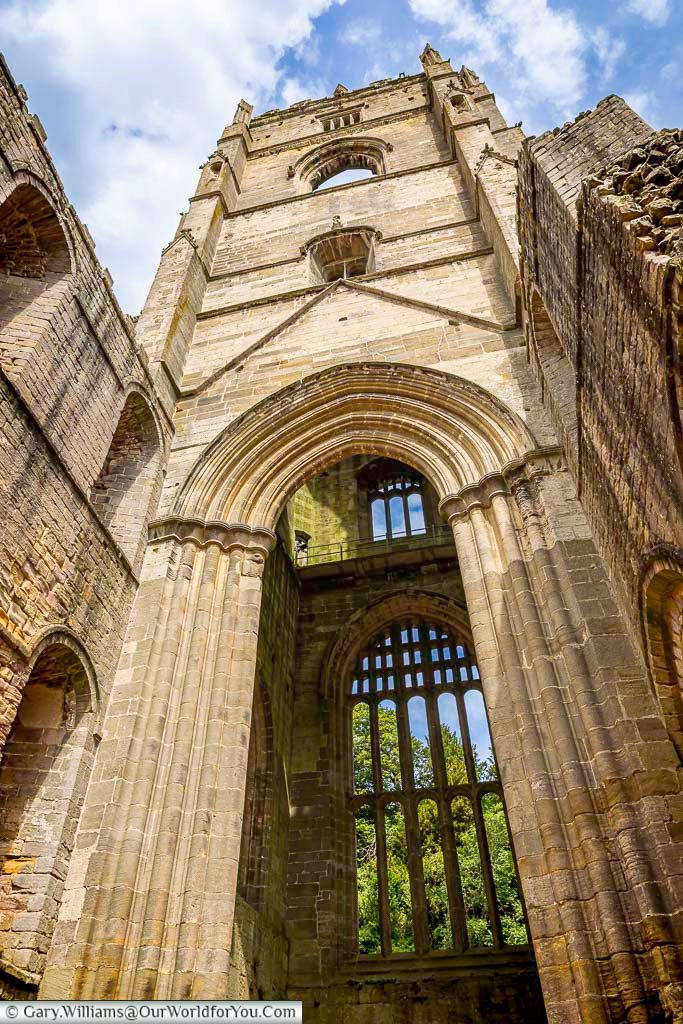 Expansive exterior view of Fountains Abbey ruins in Yorkshire, with visitors relaxing on the grass beside the towering medieval structure. The centuries-old abbey is one of the most famous historic sites in England and a highlight of exploring hidden Yorkshire landmarks.