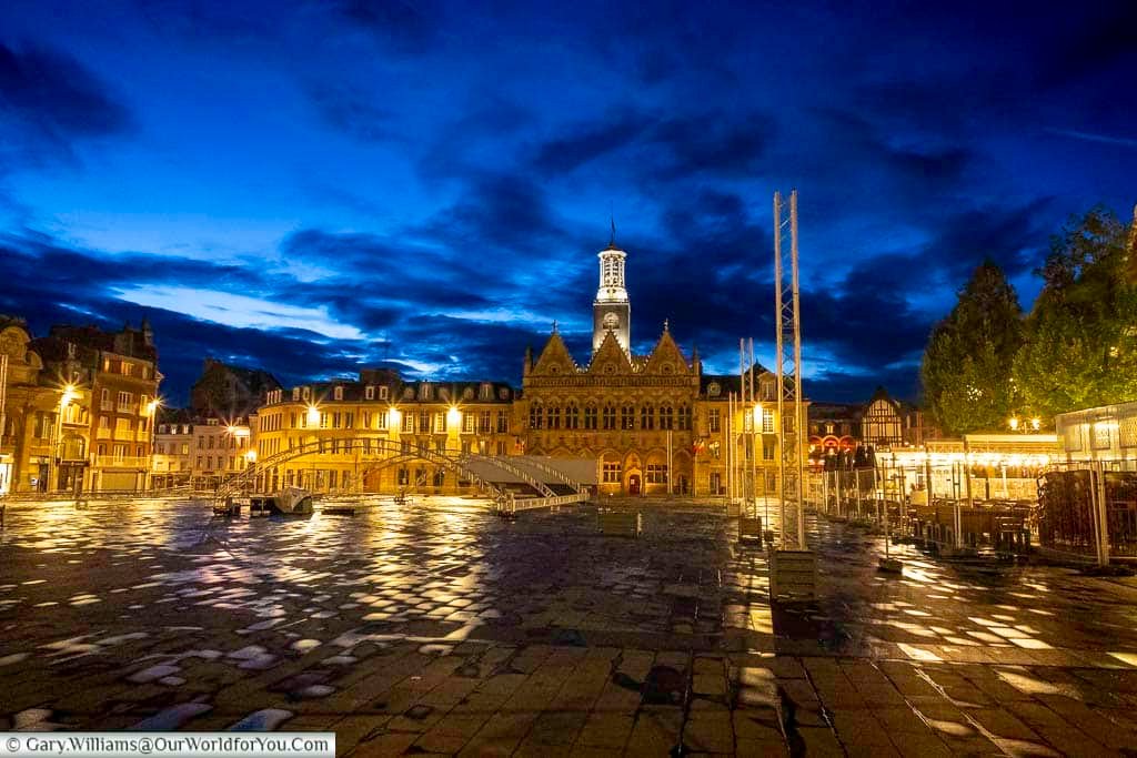 The illuminated Place de l’Hôtel de Ville in Saint-Quentin glows beautifully at night, with reflections shimmering across the rain-soaked square beneath dramatic evening skies. This atmospheric cityscape highlights the charm of Saint-Quentin after dark and is a stunning stop on any northern France walking tour or city break itinerary.