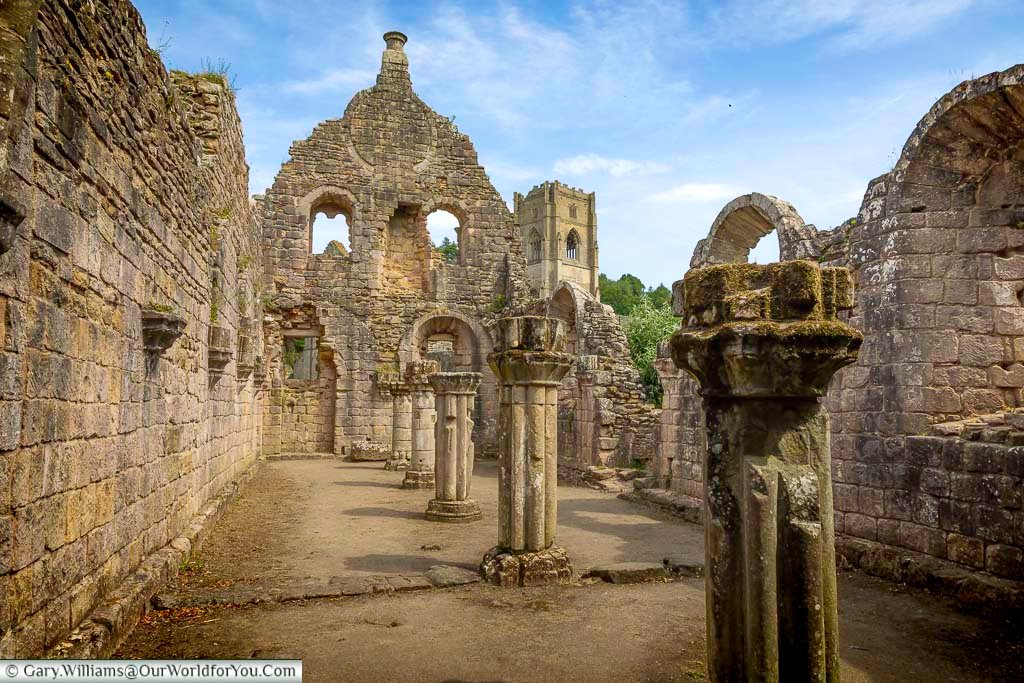 Atmospheric ruins of the Hospitium at Fountains Abbey in North Yorkshire, with ancient stone walls, weathered columns and the abbey tower rising in the distance. This medieval guesthouse ruin is one of the most intriguing hidden gems for visitors touring historic Yorkshire sites.