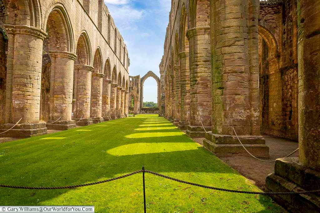 Wide view of the nave at Fountains Abbey in North Yorkshire, with towering stone columns and open grassy floors surrounded by medieval ruins. The peaceful atmosphere and remarkable architecture make this UNESCO World Heritage Site one of the top hidden gems in Yorkshire.