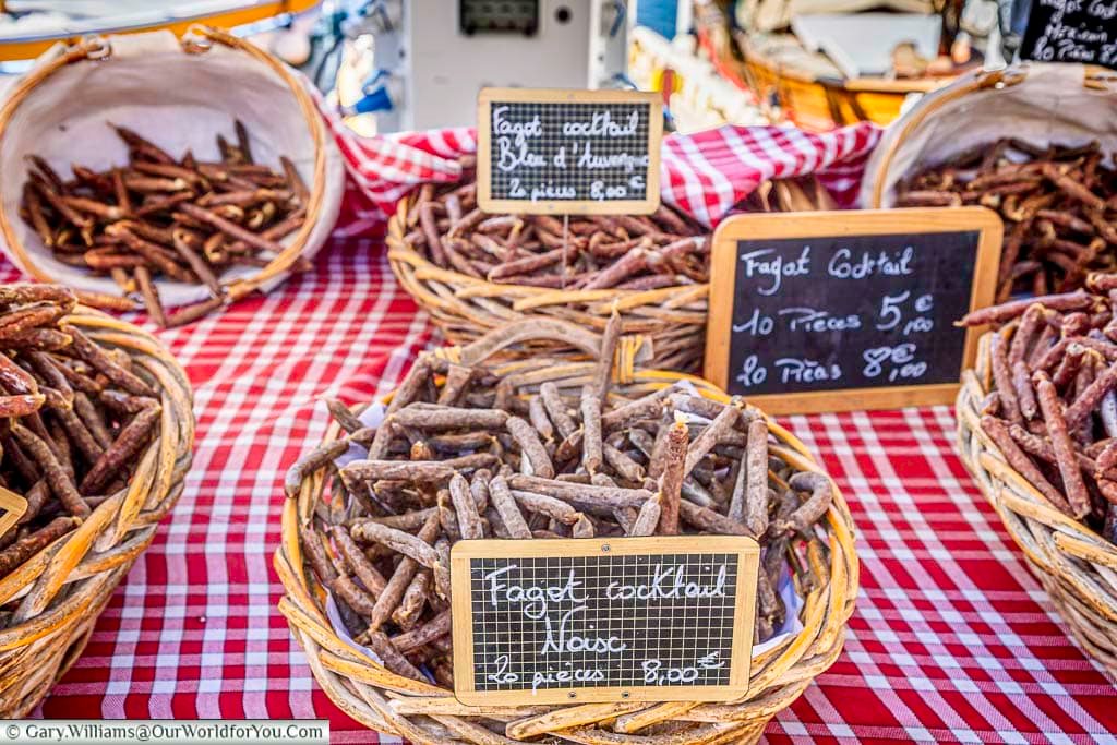 Baskets of traditional French saucisson displayed on a red-and-white checked cloth at Sanary-sur-Mer market, capturing the flavours and character of a Provençal market.