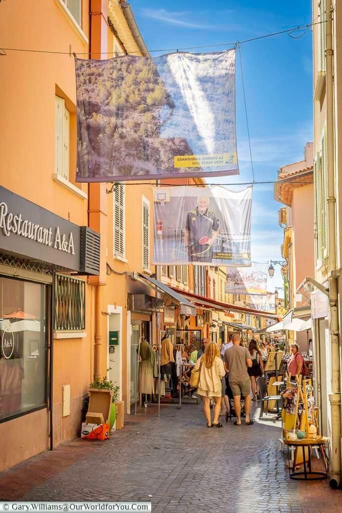 A bustling pedestrian street in Sanary-sur-Mer’s old town, lined with independent shops, restaurants and colourful Provençal buildings.