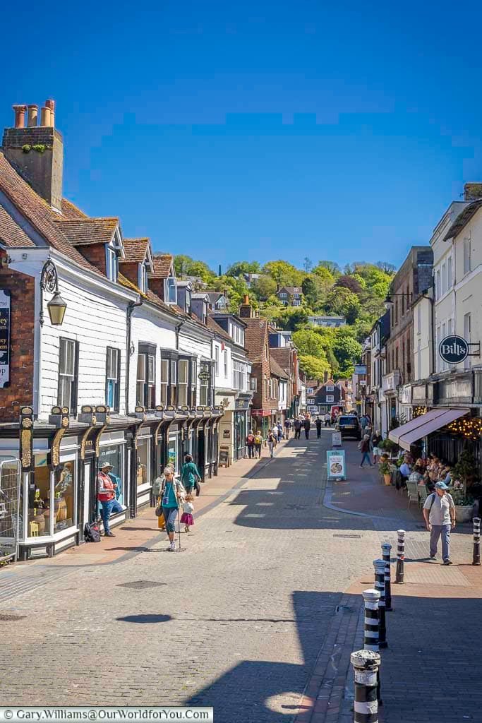 A lively view along Cliffe High Street, with independent shops, historic buildings and the green slopes surrounding Lewes rising beautifully in the distance.