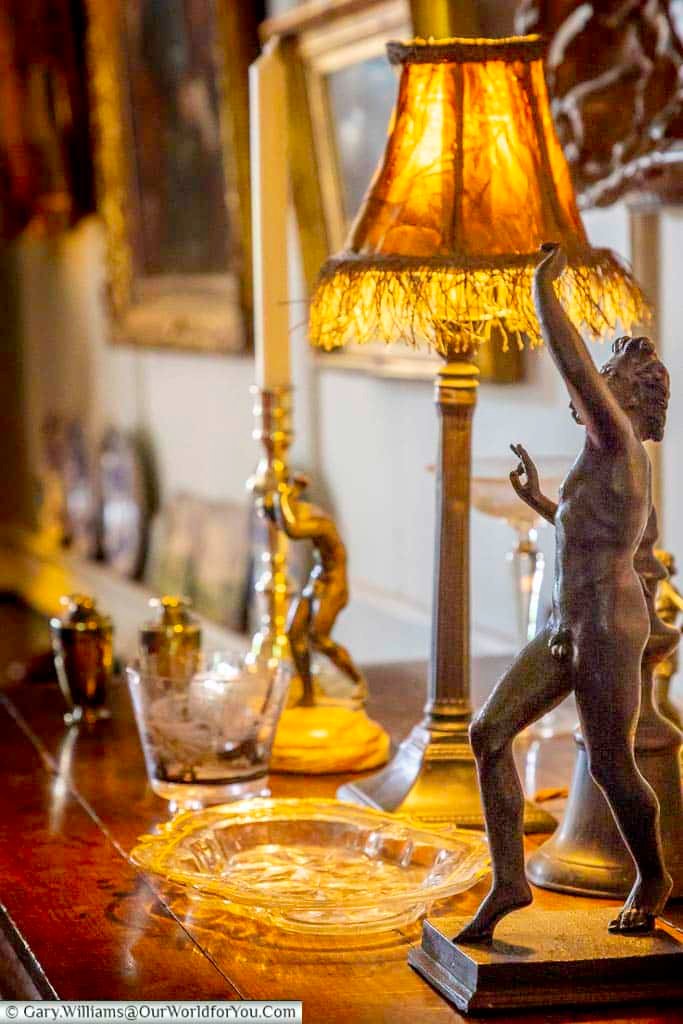 An intimate interior detail at Restoration House, with a glowing vintage table lamp, decorative glassware and a classical bronze figure creating a warm historic atmosphere.