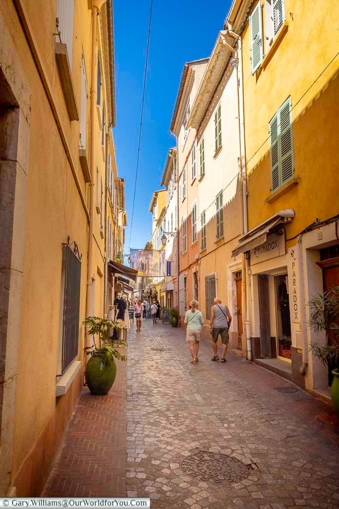 A charming pedestrian lane through Sanary-sur-Mer’s old town, lined with colourful Provençal buildings, shutters, shops and cafés.