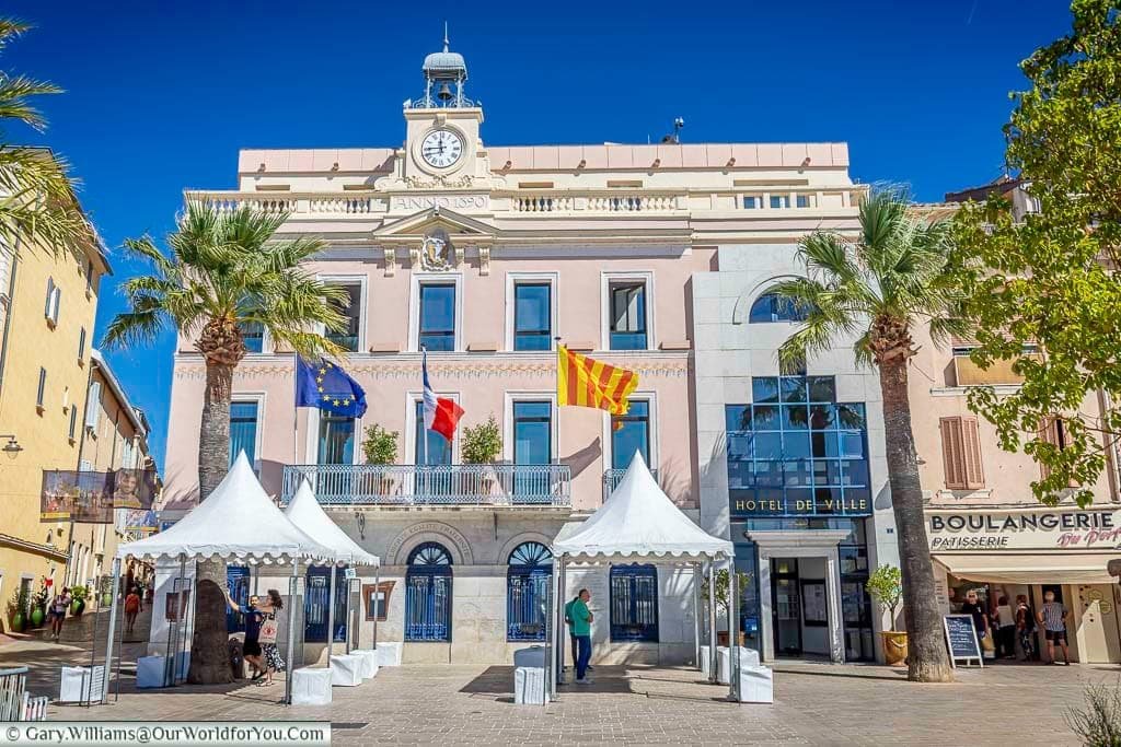 The elegant Hôtel de Ville in the heart of Sanary-sur-Mer, framed by palm trees and flying the French, European and Provençal flags.