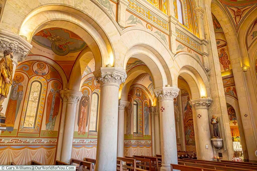 The richly decorated interior of Saint-Nazaire Church in Sanary-sur-Mer, with Romanesque-style arches and colourful religious frescoes covering the walls and vaults.
