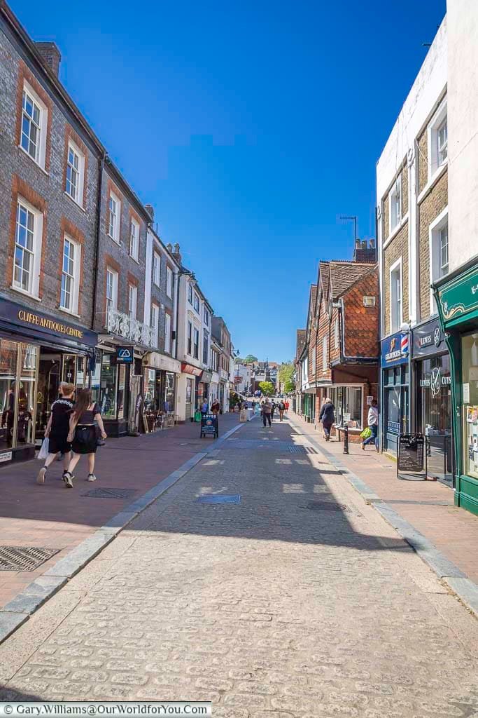 Looking along bustling Cliffe High Street towards Cliffe Bridge, lined with independent shops and historic buildings beneath a brilliant blue sky.