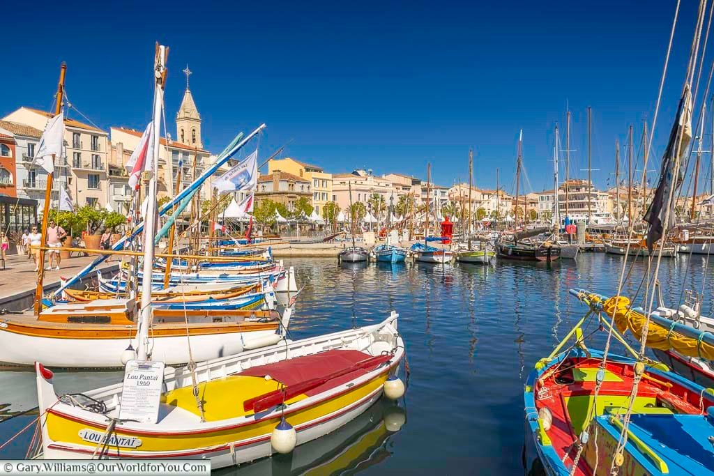 Traditional wooden boats in Sanary-sur-Mer harbour, with the bright red Portissol boat in the foreground and the waterfront beyond.