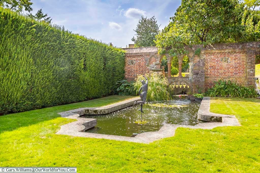 The beautifully designed garden pond at Restoration House in Rochester, shaped like a Queen Anne mirror and surrounded by immaculate lawns, hedges and historic brickwork.