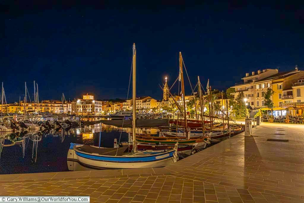 Traditional fishing boats moored in the illuminated harbour at Sanary-sur-Mer, with waterfront buildings and reflections glowing across the calm water.