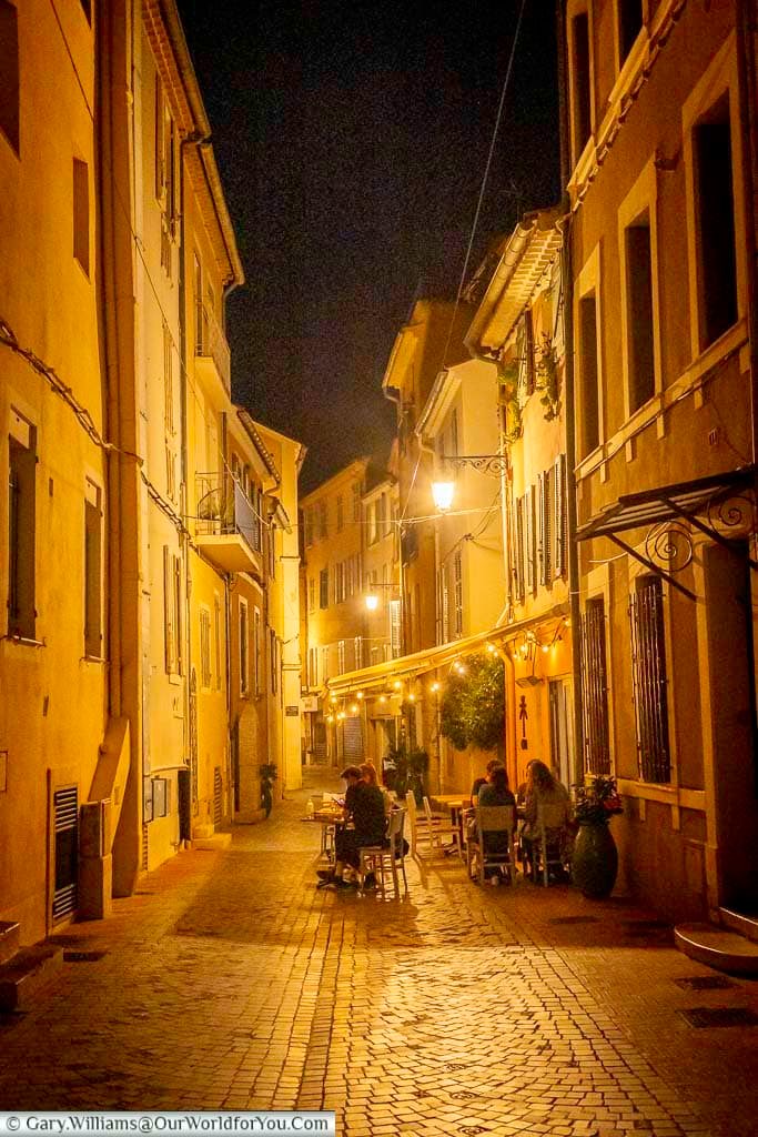 A narrow cobbled lane in Sanary-sur-Mer’s historic centre, warmly illuminated at night with diners enjoying an intimate pavement restaurant.