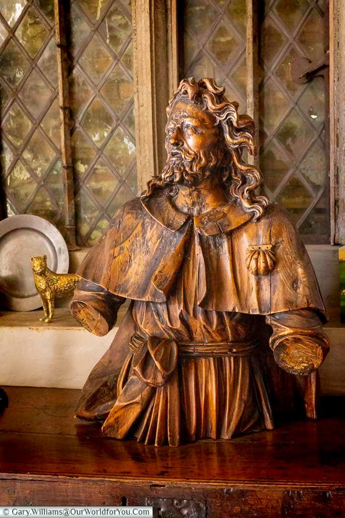 Historic carved wooden statue displayed at Restoration House in Rochester, Kent, set against an atmospheric leaded-glass window and surrounded by period objects.