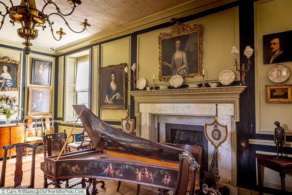 The elegant Great Chamber at Restoration House in Rochester, featuring a historic keyboard instrument, marble fireplace, antique furniture and an extensive collection of portraits.