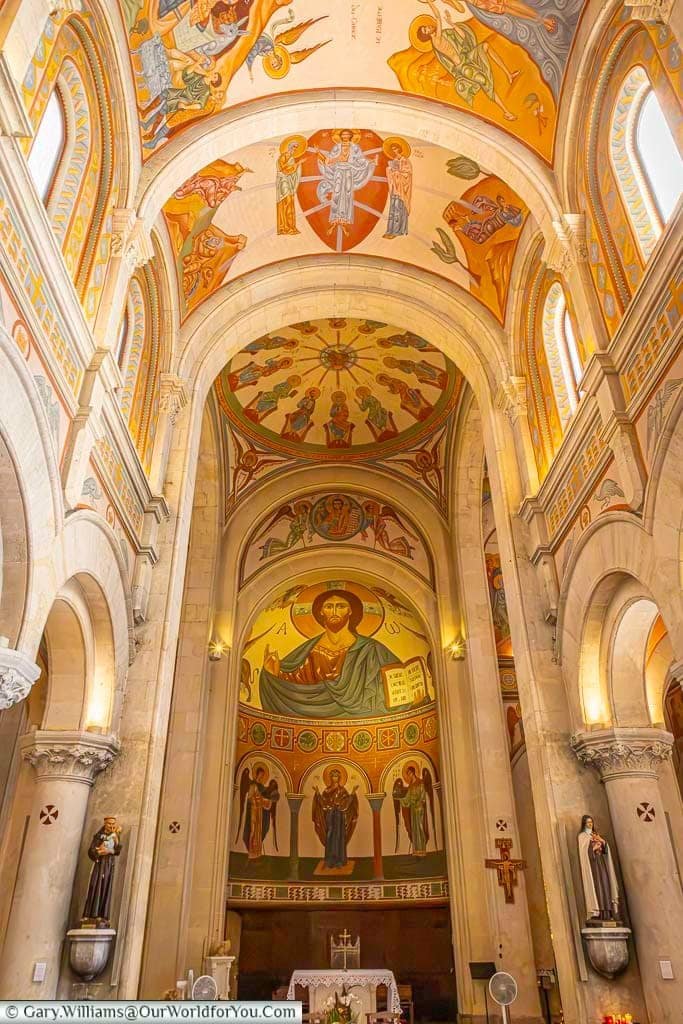 Looking along the soaring nave of Saint-Nazaire Church in Sanary-sur-Mer towards the altar, surrounded by colourful biblical murals and decorative arches.