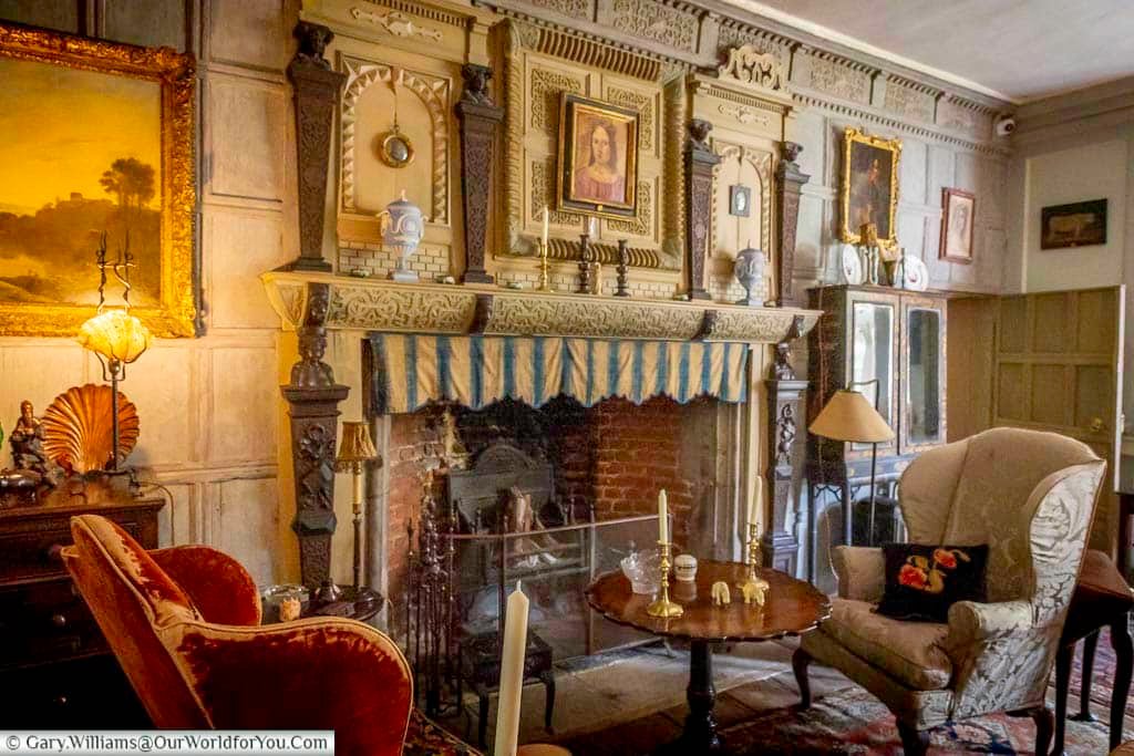 The characterful Oak Saloon at Restoration House in Rochester, featuring an ornate carved fireplace, period furniture, paintings and historic wood panelling.