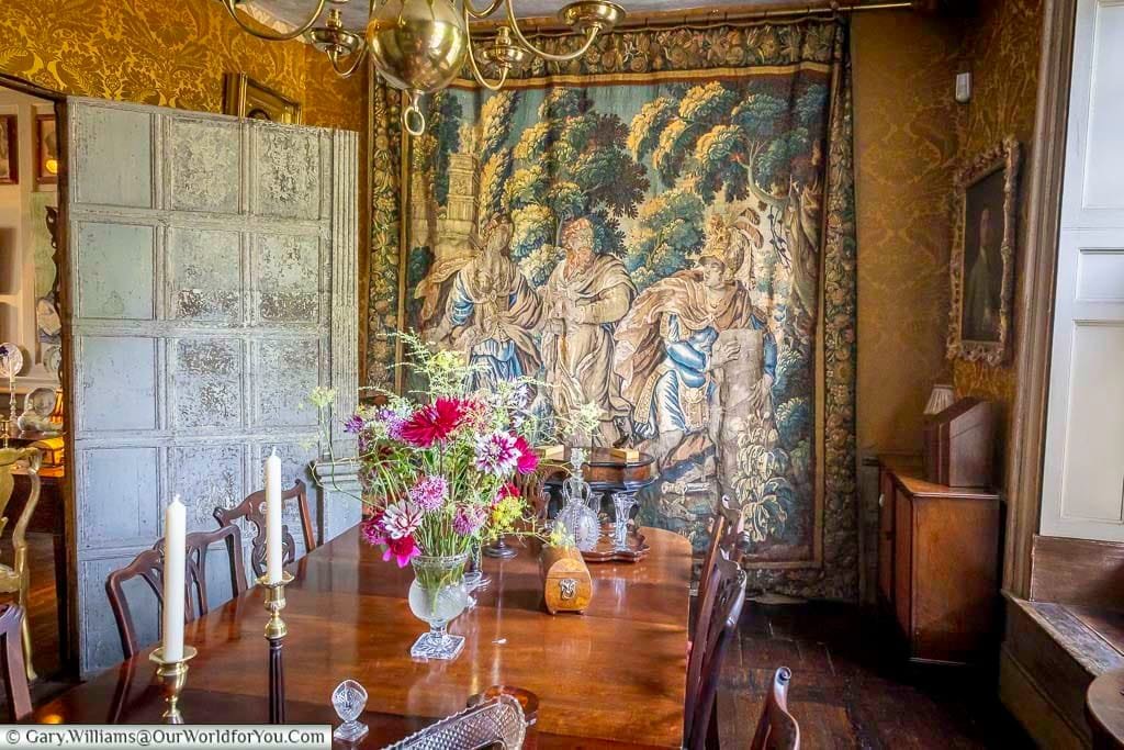 The atmospheric Tapestry Room at Restoration House in Rochester, Kent, featuring an impressive historic tapestry, polished dining table, antique furniture and a colourful arrangement of garden flowers.