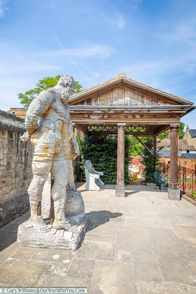 Top terrace of the Restoration House gardens in Rochester, featuring a striking sculptural figure beside a timber pavilion overlooking the landscaped grounds.