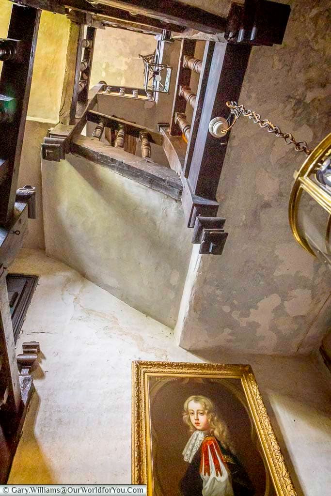 Looking upwards through the atmospheric timber winding staircase at Restoration House, with a historic portrait displayed beneath the old wooden balustrades.