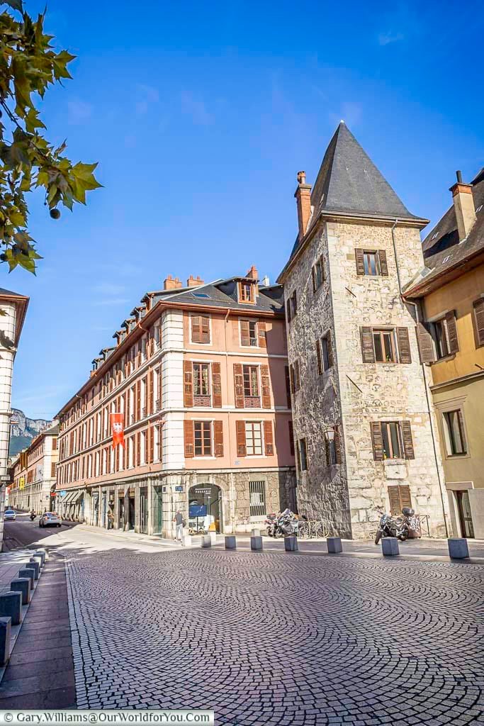 A tall stone tower with a steeply pitched roof stands among the historic buildings close to Place du Château in Chambéry. Cobbled streets, colourful façades and surviving medieval architecture give this part of the city its distinctive Savoyard character.
