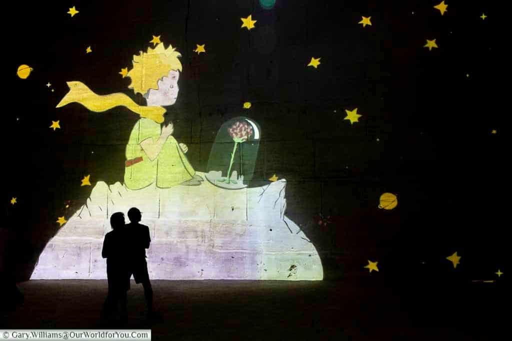 The Little Prince surrounded by stars in an immersive projection across the limestone walls of Carrières des Lumières in Provence.
