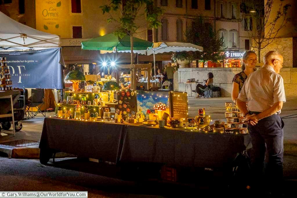Illuminated stall selling handmade ornaments and decorative crafts at the summer night market in Saint-Rémy-de-Provence, France.