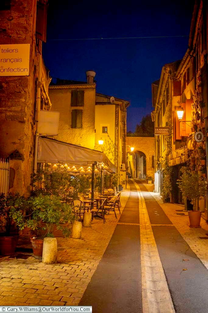 Atmospheric illuminated street lined with cafés and historic stone buildings during an evening stroll through Saint-Rémy-de-Provence.